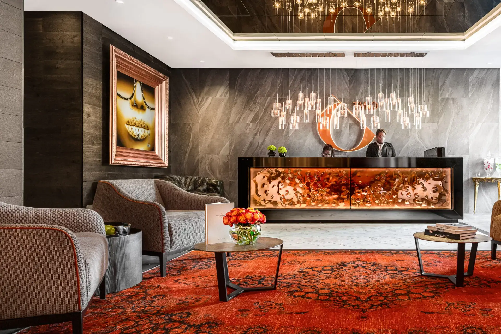 Employees workign at the front desk of a reception area with seating, a red carpet, hanging lights and artwork